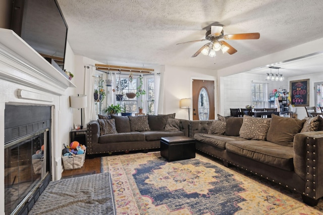 living room with ceiling fan with notable chandelier, wood-type flooring, and a textured ceiling