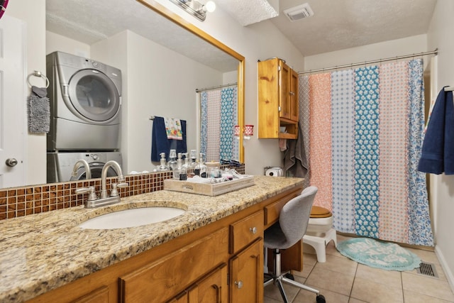 bathroom with toilet, stacked washer / drying machine, tile patterned flooring, and a textured ceiling