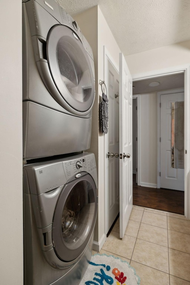 laundry area with a textured ceiling, stacked washer / dryer, and light tile patterned floors