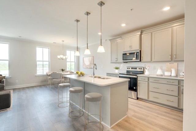 kitchen featuring a kitchen island with sink, sink, light hardwood / wood-style flooring, appliances with stainless steel finishes, and decorative light fixtures