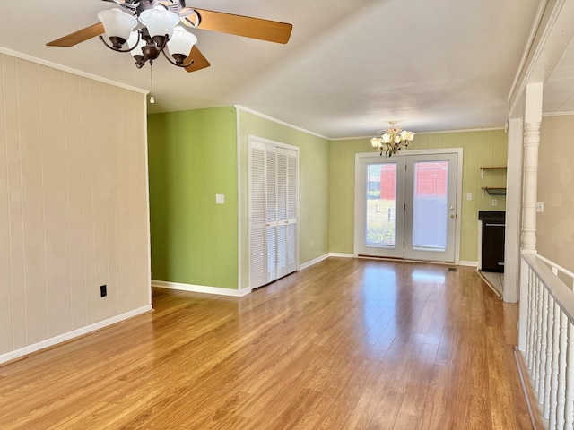 unfurnished living room featuring ceiling fan with notable chandelier, wood walls, ornamental molding, and light hardwood / wood-style flooring