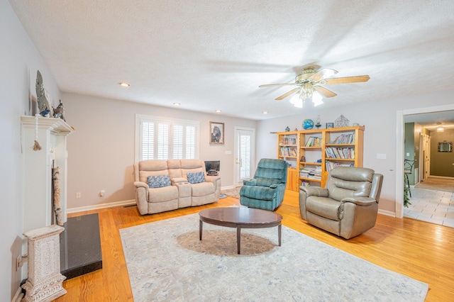 living room featuring ceiling fan, a fireplace, wood-type flooring, and a textured ceiling