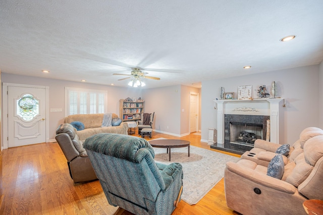 living room with a fireplace, a textured ceiling, light wood-type flooring, and ceiling fan