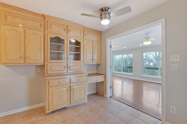 kitchen with light brown cabinetry, built in desk, light hardwood / wood-style flooring, and ceiling fan