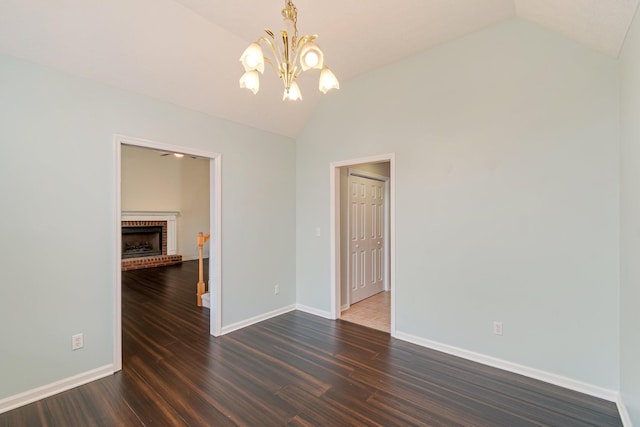 unfurnished room with a fireplace, dark hardwood / wood-style flooring, vaulted ceiling, and an inviting chandelier