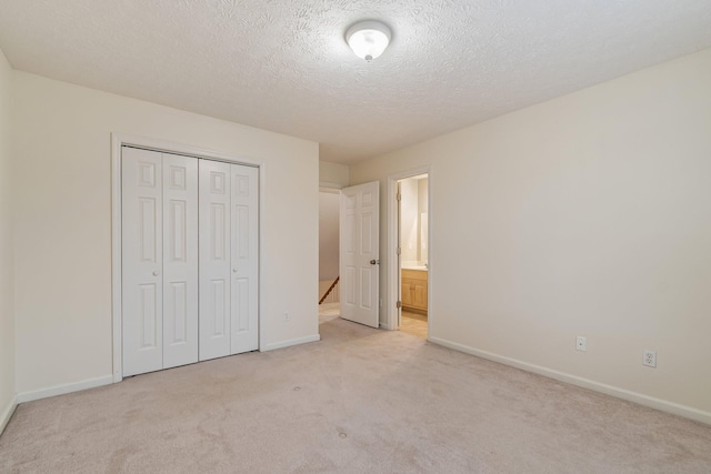 unfurnished bedroom featuring ensuite bath, light carpet, a closet, and a textured ceiling