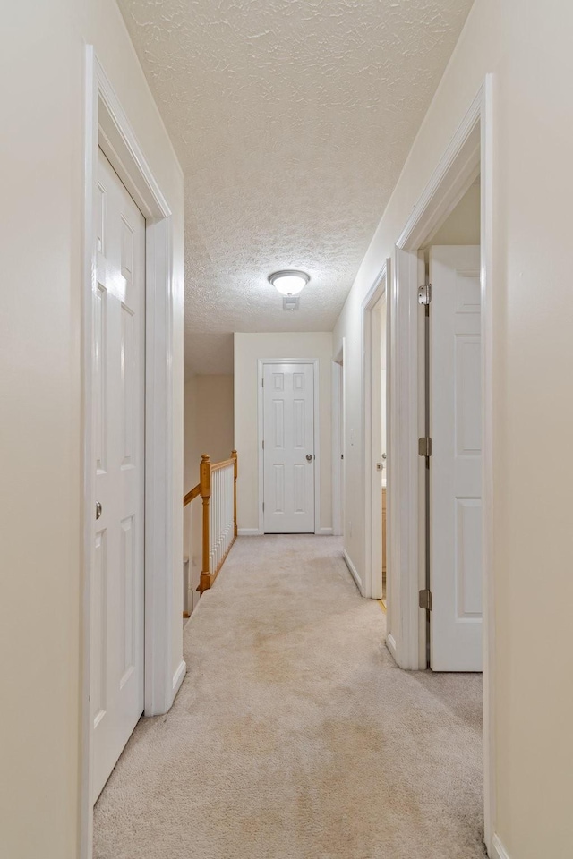 corridor with light carpet and a textured ceiling