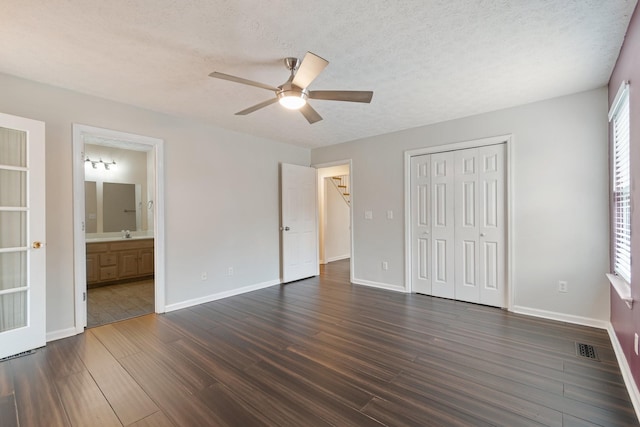 unfurnished bedroom with ceiling fan, dark wood-type flooring, connected bathroom, and a closet