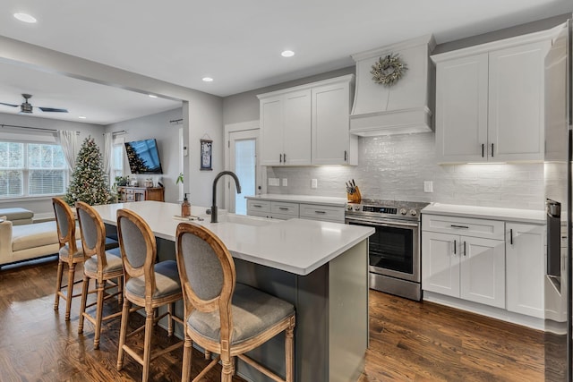 kitchen featuring premium range hood, dark wood-type flooring, white cabinetry, stainless steel range with electric cooktop, and an island with sink