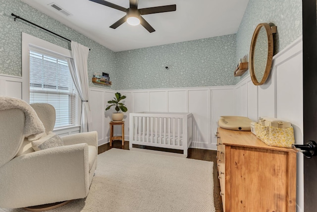 bedroom featuring a nursery area, hardwood / wood-style flooring, and ceiling fan