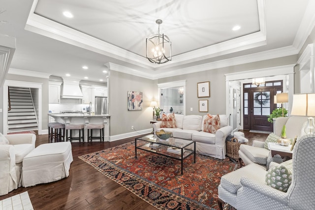 living room featuring ornamental molding, dark hardwood / wood-style flooring, a tray ceiling, and a notable chandelier