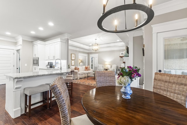 dining room with ornamental molding, a tray ceiling, sink, a notable chandelier, and dark hardwood / wood-style floors