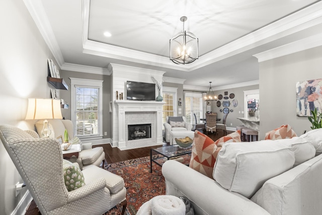 living room with a raised ceiling, dark hardwood / wood-style flooring, crown molding, a chandelier, and a fireplace