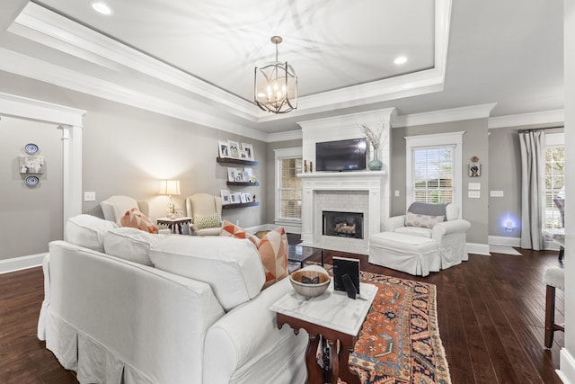 living room with a raised ceiling, crown molding, an inviting chandelier, a fireplace, and dark hardwood / wood-style floors