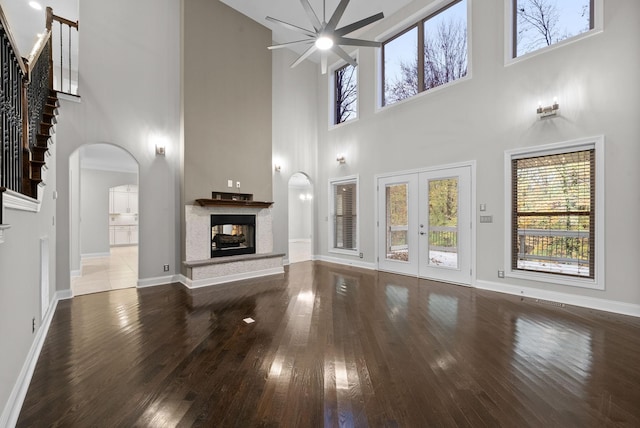 unfurnished living room featuring french doors, a towering ceiling, ceiling fan, wood-type flooring, and a multi sided fireplace