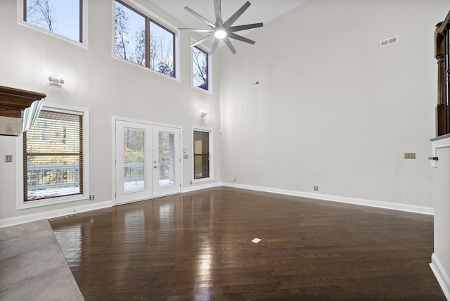 unfurnished living room featuring a towering ceiling, dark hardwood / wood-style floors, and plenty of natural light