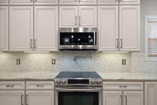 kitchen featuring white cabinets, backsplash, light stone counters, and stainless steel appliances