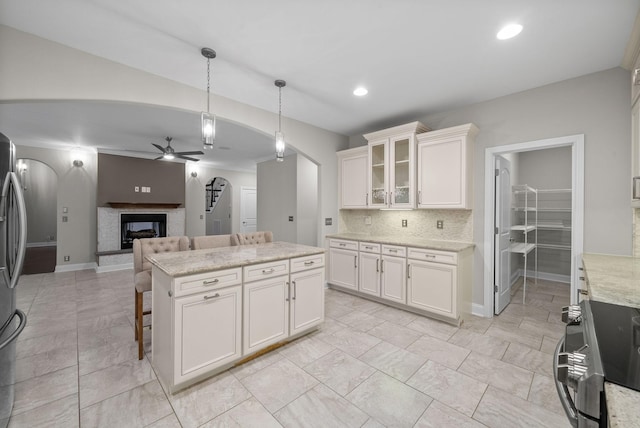 kitchen featuring range, a multi sided fireplace, ceiling fan, decorative light fixtures, and white cabinetry