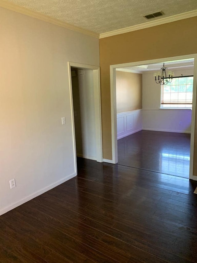 empty room featuring ornamental molding, dark wood-type flooring, a textured ceiling, and an inviting chandelier