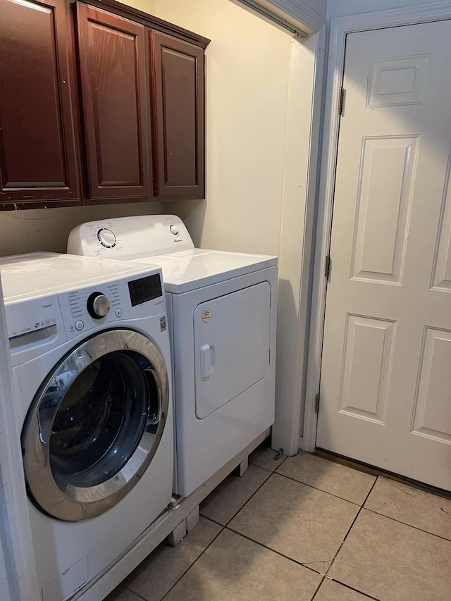 clothes washing area featuring washer and dryer, cabinets, and light tile patterned floors