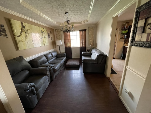 living room with dark hardwood / wood-style floors, ornamental molding, a textured ceiling, a tray ceiling, and a chandelier