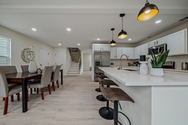 kitchen featuring decorative backsplash, stainless steel appliances, sink, white cabinetry, and hanging light fixtures