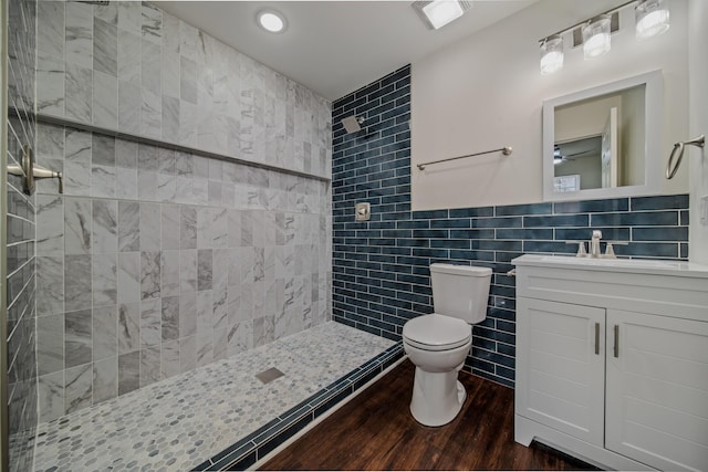 bathroom with a tile shower, toilet, vanity, tile walls, and hardwood / wood-style flooring