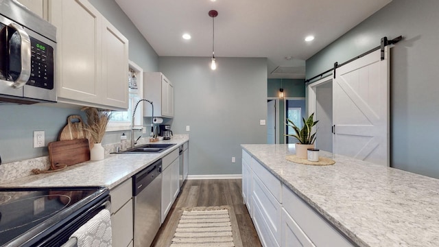 kitchen with appliances with stainless steel finishes, sink, pendant lighting, a barn door, and white cabinetry