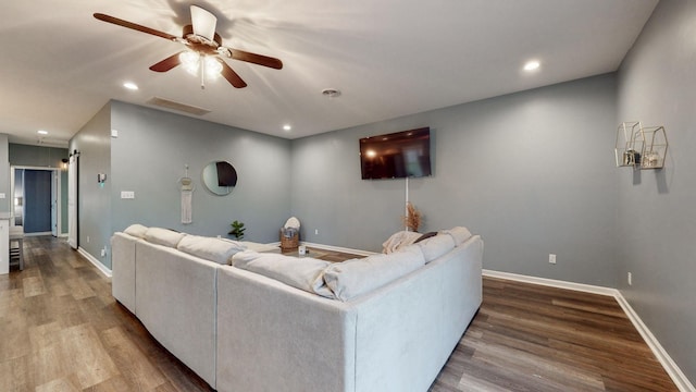 living room with ceiling fan, a barn door, and wood-type flooring