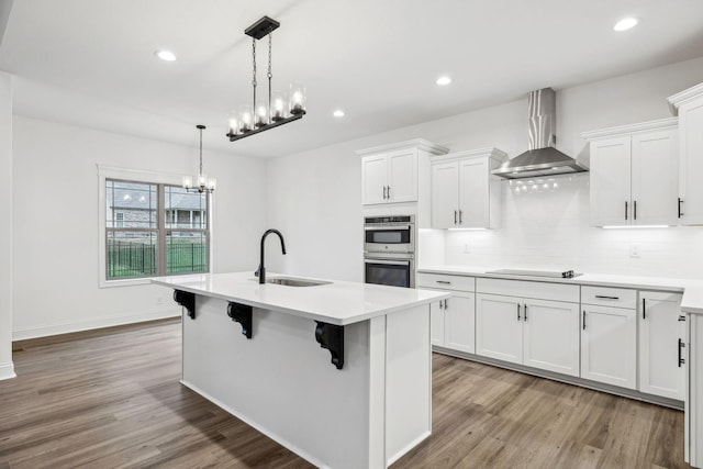 kitchen with white cabinetry, sink, wall chimney range hood, and hardwood / wood-style flooring