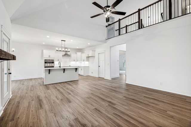 unfurnished living room featuring ceiling fan with notable chandelier, a towering ceiling, light hardwood / wood-style flooring, and sink