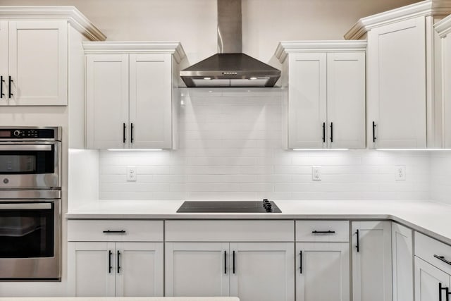 kitchen with backsplash, wall chimney exhaust hood, stainless steel double oven, black electric cooktop, and white cabinets