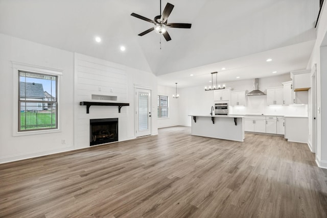 unfurnished living room featuring ceiling fan with notable chandelier, a large fireplace, sink, high vaulted ceiling, and light hardwood / wood-style flooring