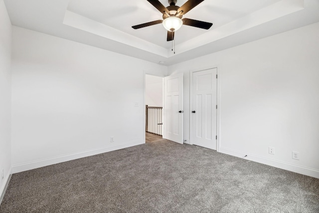 unfurnished room featuring dark colored carpet, ceiling fan, and a tray ceiling