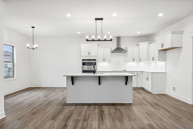 kitchen featuring white cabinets, an island with sink, light hardwood / wood-style flooring, and wall chimney range hood