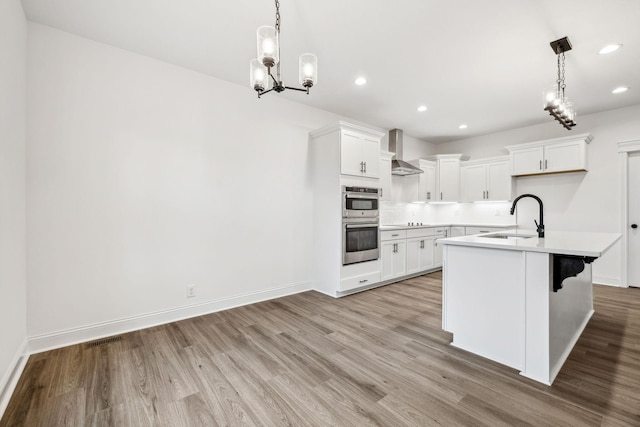 kitchen with wall chimney range hood, white cabinetry, light hardwood / wood-style flooring, and sink