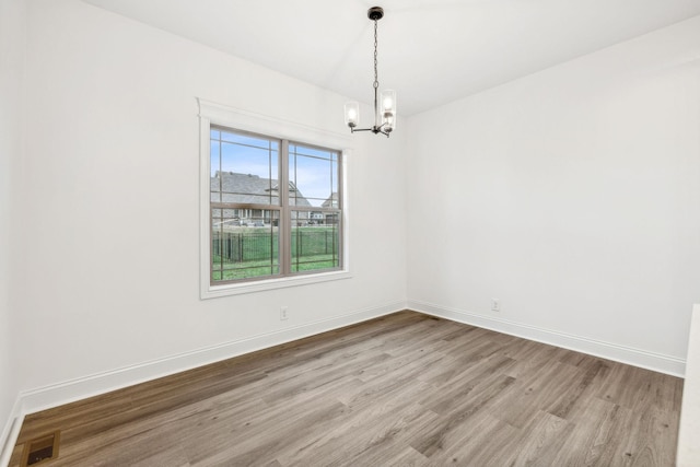 spare room with light hardwood / wood-style flooring and a chandelier