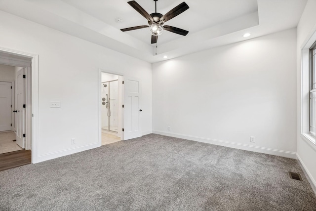 unfurnished bedroom featuring a raised ceiling, ensuite bath, ceiling fan, and light carpet