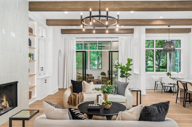 living room featuring beam ceiling, a fireplace, a notable chandelier, and light hardwood / wood-style flooring