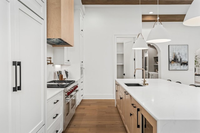 kitchen with a kitchen island with sink, white cabinets, hanging light fixtures, light hardwood / wood-style flooring, and beamed ceiling