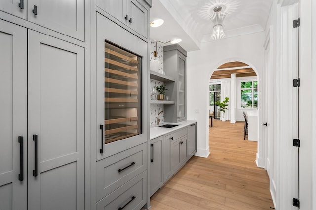 bar with decorative light fixtures, gray cabinets, beverage cooler, and light hardwood / wood-style floors