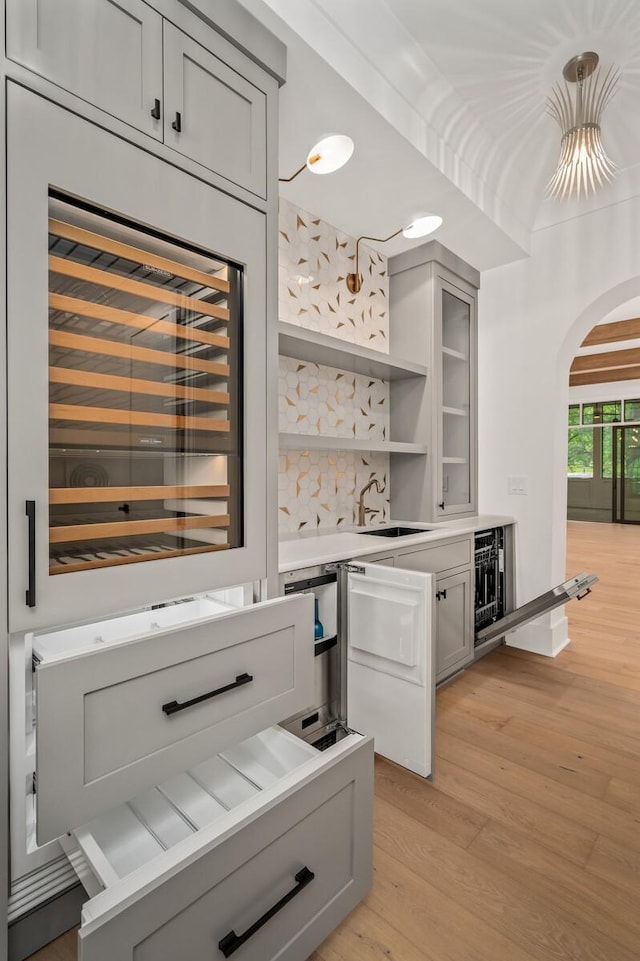 bar featuring hanging light fixtures, decorative backsplash, gray cabinets, light wood-type flooring, and beverage cooler