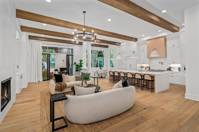 living room featuring light wood-type flooring, sink, beam ceiling, an inviting chandelier, and a fireplace