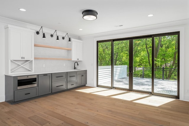 bar featuring white cabinetry, sink, tasteful backsplash, light hardwood / wood-style flooring, and gray cabinets