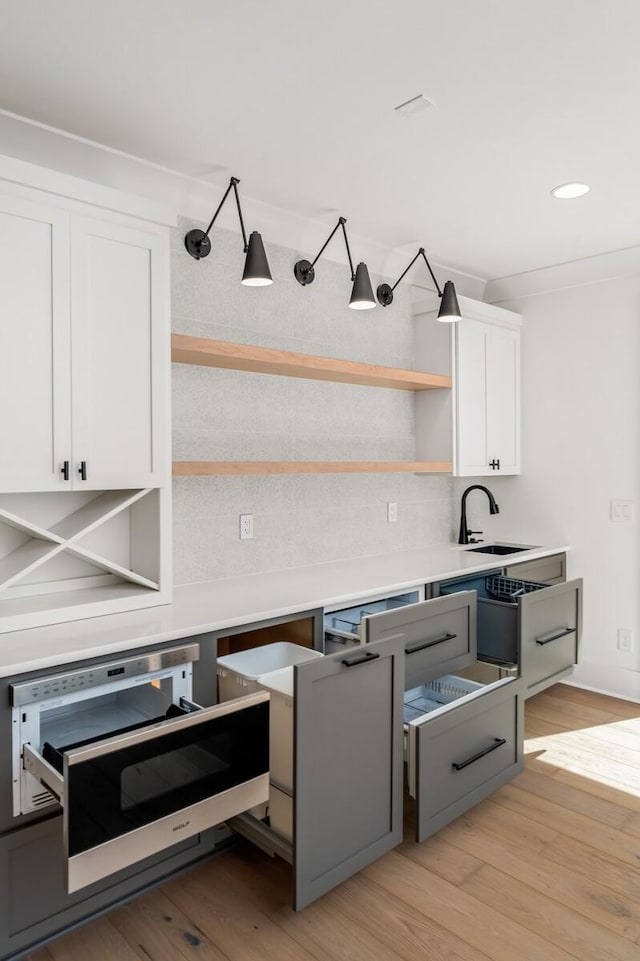 kitchen with backsplash, light hardwood / wood-style floors, white cabinetry, and sink