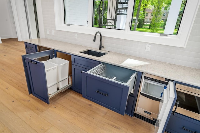 kitchen featuring blue cabinetry, light stone countertops, sink, and light wood-type flooring