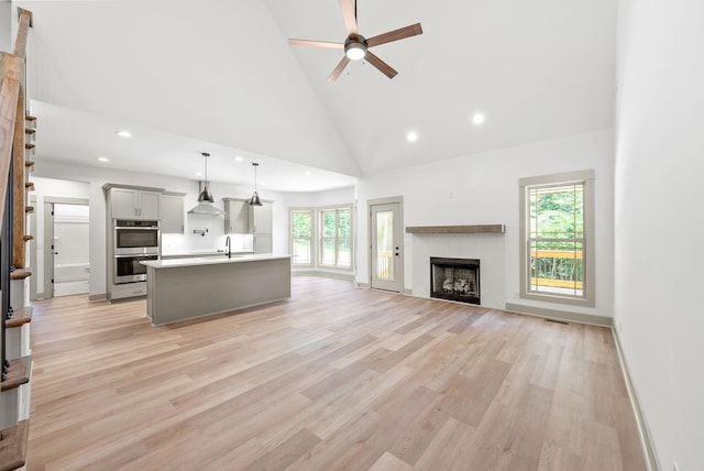 unfurnished living room with ceiling fan, sink, high vaulted ceiling, and light hardwood / wood-style flooring