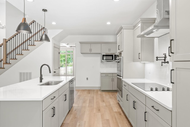 kitchen featuring a kitchen island with sink, sink, light hardwood / wood-style flooring, wall chimney exhaust hood, and appliances with stainless steel finishes