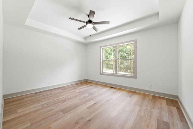 unfurnished room featuring a raised ceiling, ceiling fan, and light wood-type flooring