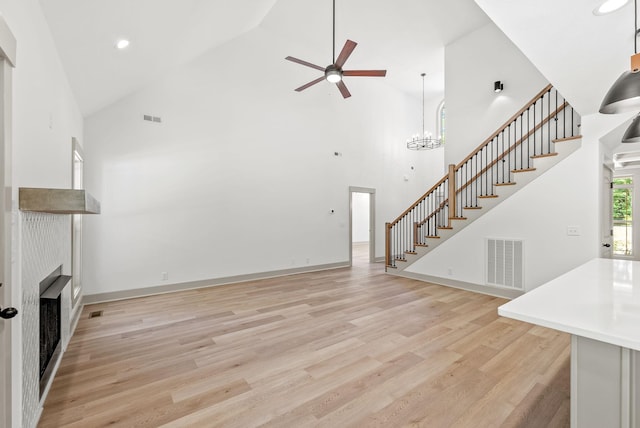 unfurnished living room with light hardwood / wood-style flooring, high vaulted ceiling, and ceiling fan with notable chandelier